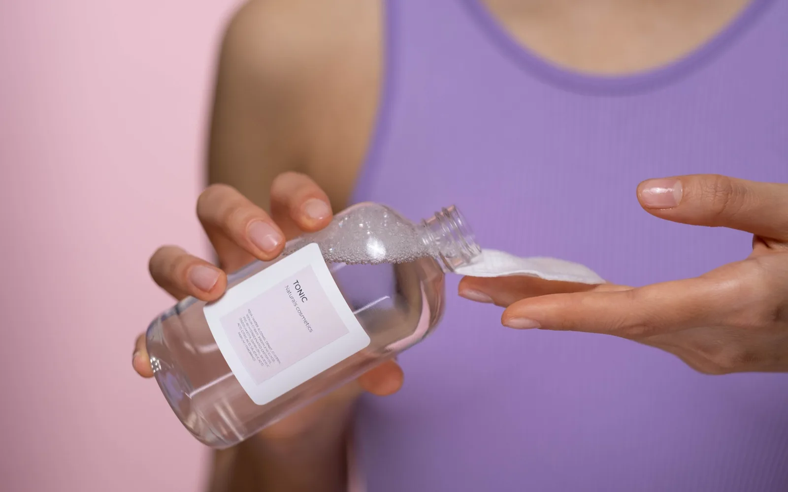 Mains qui versent une lotion tonique sur un coton avant de l’appliquer sur la peau.