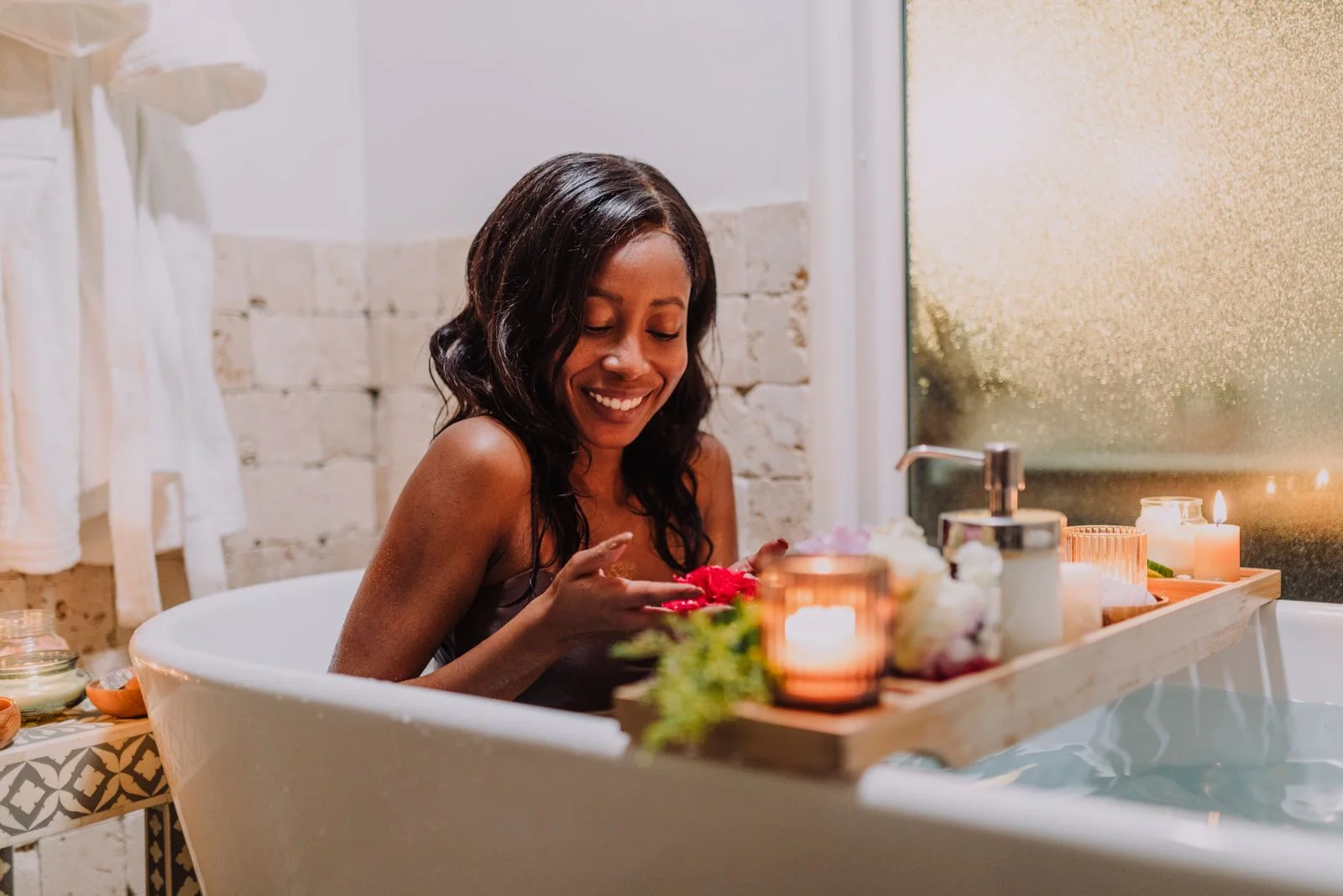 Femme dans un bain chaud du soir, plateau posé sur la baignoire et bougies allumées.