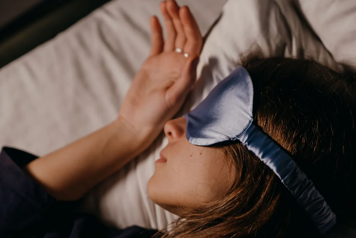 Femme endormie, masque de nuit en soie sur les yeux, la main posée sur l’oreiller.