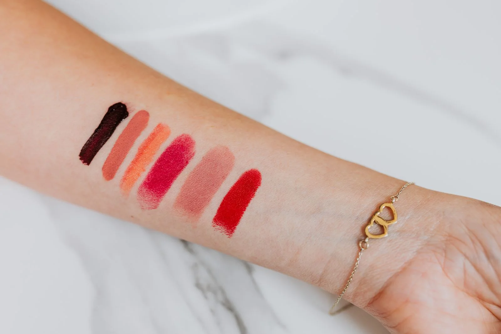 Six essais de rouge à lèvres alignés sur l’intérieur d’un poignet, du nude au rouge vif.